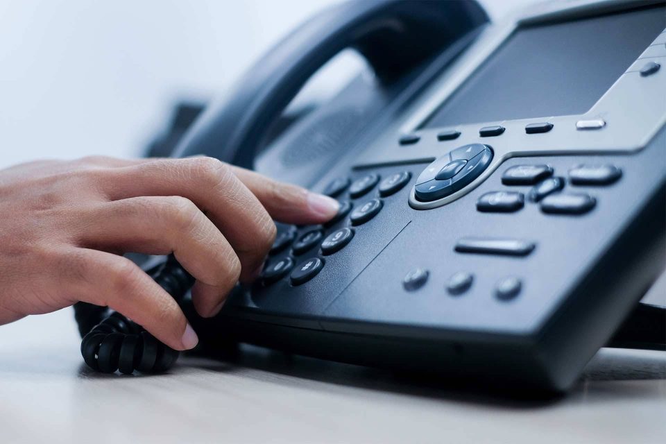 Hand pressing buttons on a landline phone in an office setting at BoneSim.