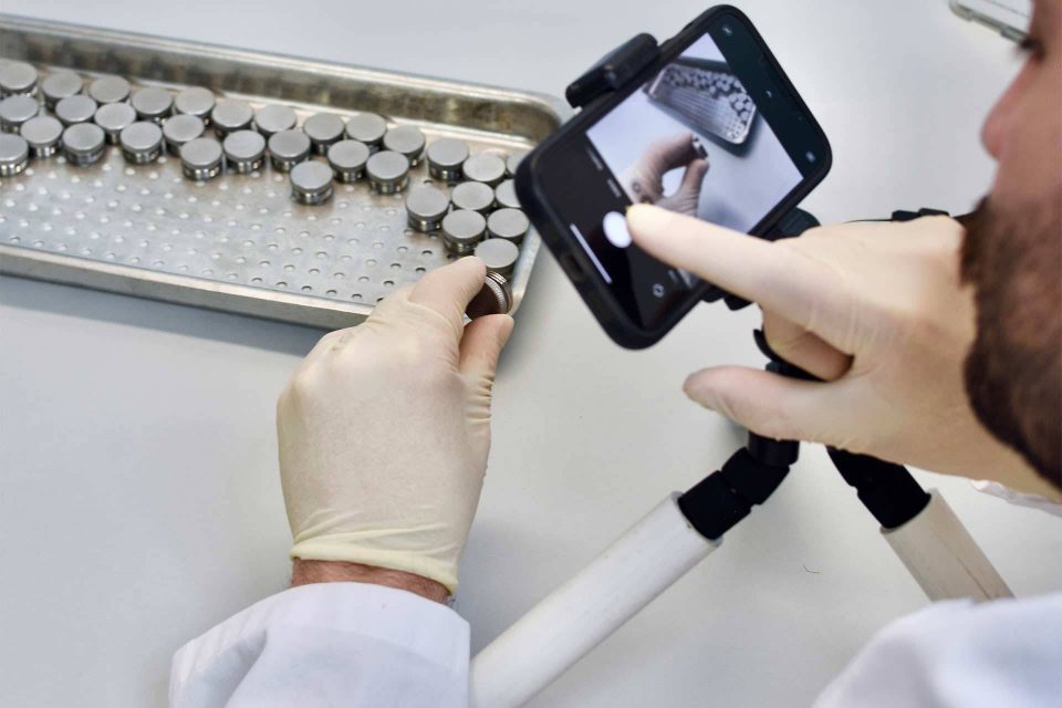 Hands in white latex gloves manually inspecting items using a phone on a tripod at BoneSim.