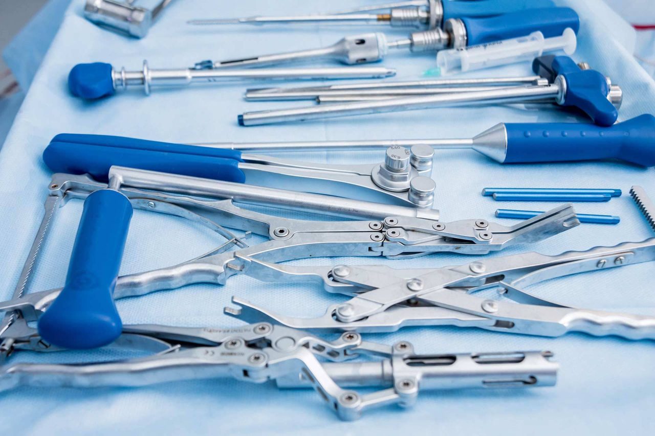 Metal medical tools with blue handles laid on pale blue cloth showcasing how BoneSim's reprocessing reusable medical devices meets regulatory compliance.